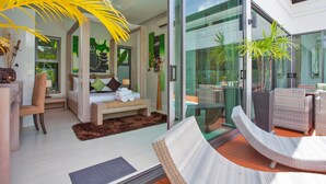 A modern living room with a sofa, a chair, a small table, and a large window. - Isawan 2BR Salt Pool Villa in Baannaraya (Rawai)