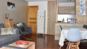A compact living space with a sofa, a dining table with chairs, a kitchen area, and a wooden door. - For rent: Central apartment, 3 rooms, ideal for family (Pralognan-la-Vanoise)