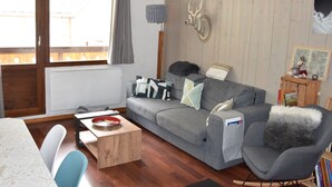 A living room with a grey sofa, a wooden coffee table, a dining table with chairs, and a wooden floor. - For rent: Central apartment, 3 rooms, ideal for family (Pralognan-la-Vanoise)