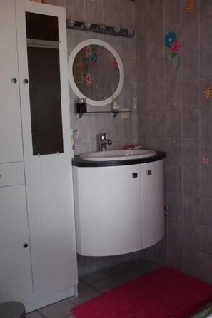 Une salle de bain avec un meuble-lavabo blanc, un miroir rond et un tapis rouge.