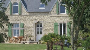A stone building with green shutters, a patio with outdoor furniture, and a small garden with palm trees. - Old house, *** privileged frame, near Pors Carn, the Torch (Penmarch)