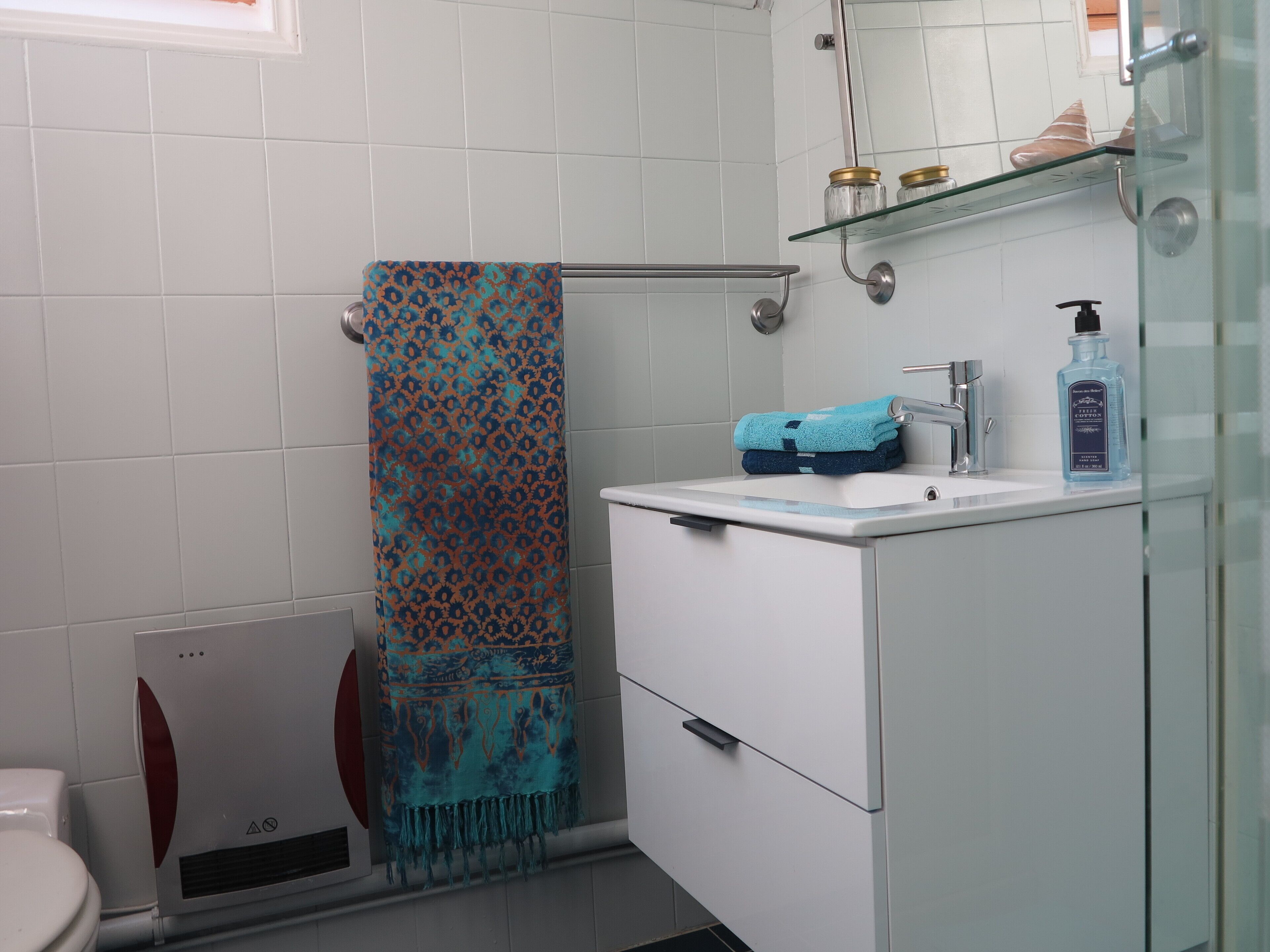 Un baño con lavamanos blanco, cabina de ducha de vidrio y toallero con una toalla estampada.