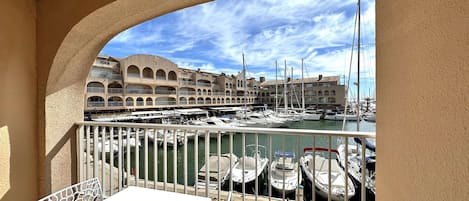 Ein Balkon mit Blick auf eine Marina, wo Boote und ein Gebäude mit bogenförmigen Balkonen zu sehen sind.