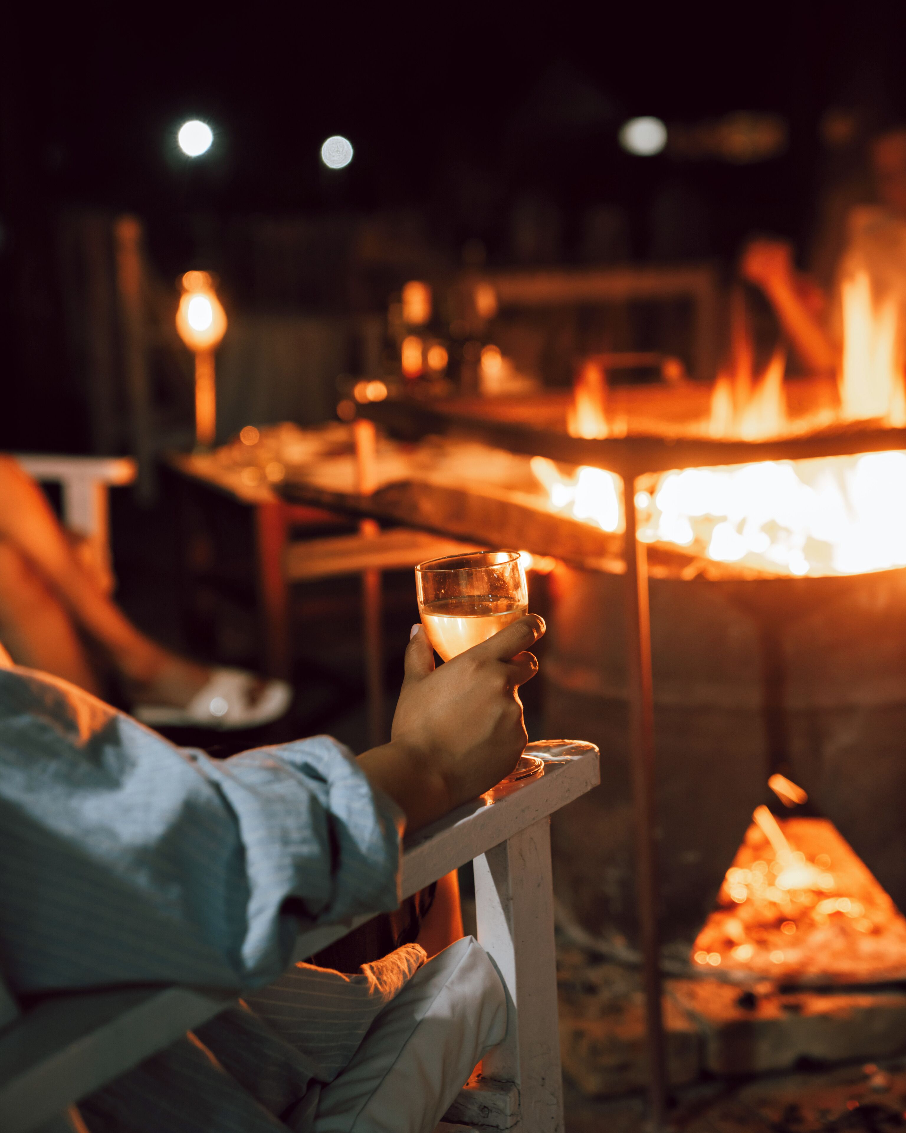 A person holding a glass near a campfire.