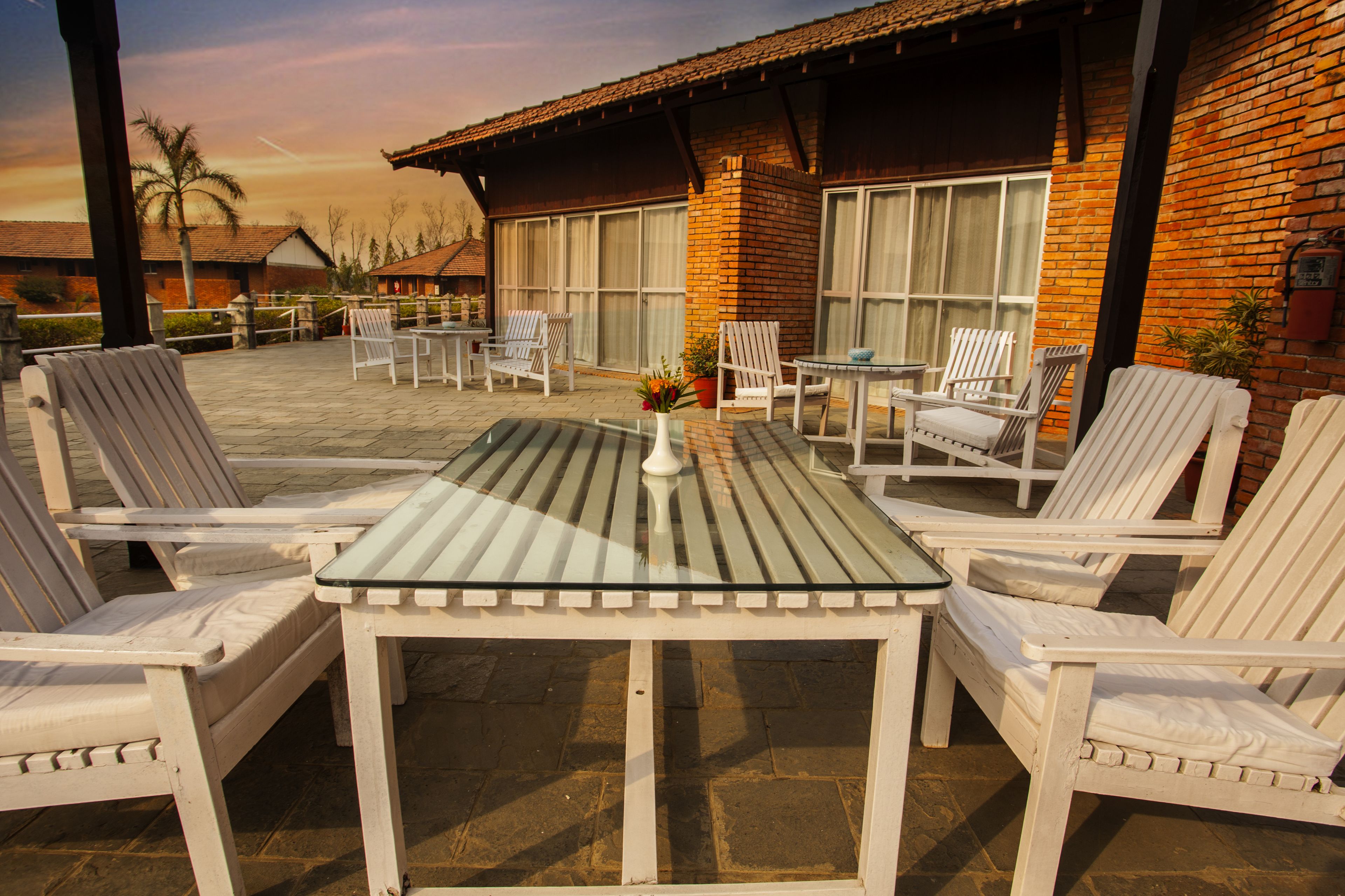 A patio area with white lounge chairs and a glass-top table, surrounded by brick walls and large windows.