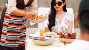 A dining table with food and drinks, a person serving food, and another person seated. - Lumbini Hokke Hotel (Sauraha Pharsatikar)