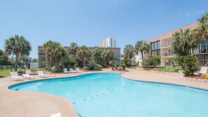 A swimming pool with lounge chairs, palm trees, and a building with balconies in the background. - Let The Waves Hit Your Feet & Sand Be Your Seat! Step Right Out To The Pool! (Biloxi)