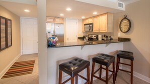 A modern kitchen with a central island, wooden cabinets, and a stainless steel microwave. - Let The Waves Hit Your Feet & Sand Be Your Seat! Step Right Out To The Pool! (Biloxi)