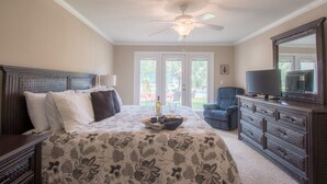 A bedroom with a large bed, a ceiling fan, a dresser, a television, and a view of the outdoors through the door. - Let The Waves Hit Your Feet & Sand Be Your Seat! Step Right Out To The Pool! (Biloxi)