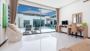 Una sala de estar moderna con un ventanal de vidrio que da a una zona de piscina, un televisor de pantalla plana y un escritorio de madera.