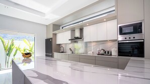 Una cocina moderna con un amplio ventanal, armarios blancos y electrodomésticos de acero inoxidable.