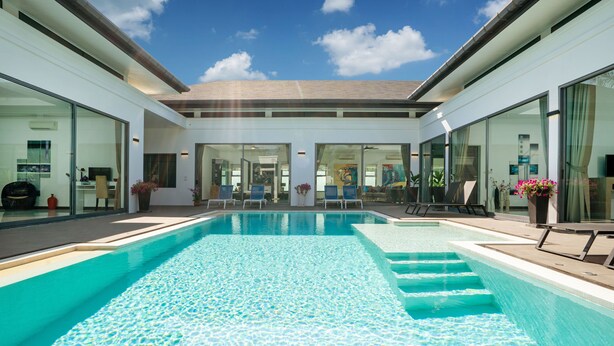 Un área de piscina moderna con agua azul cristalina, sillas de descanso y puertas de vidrio que dan a un edificio.