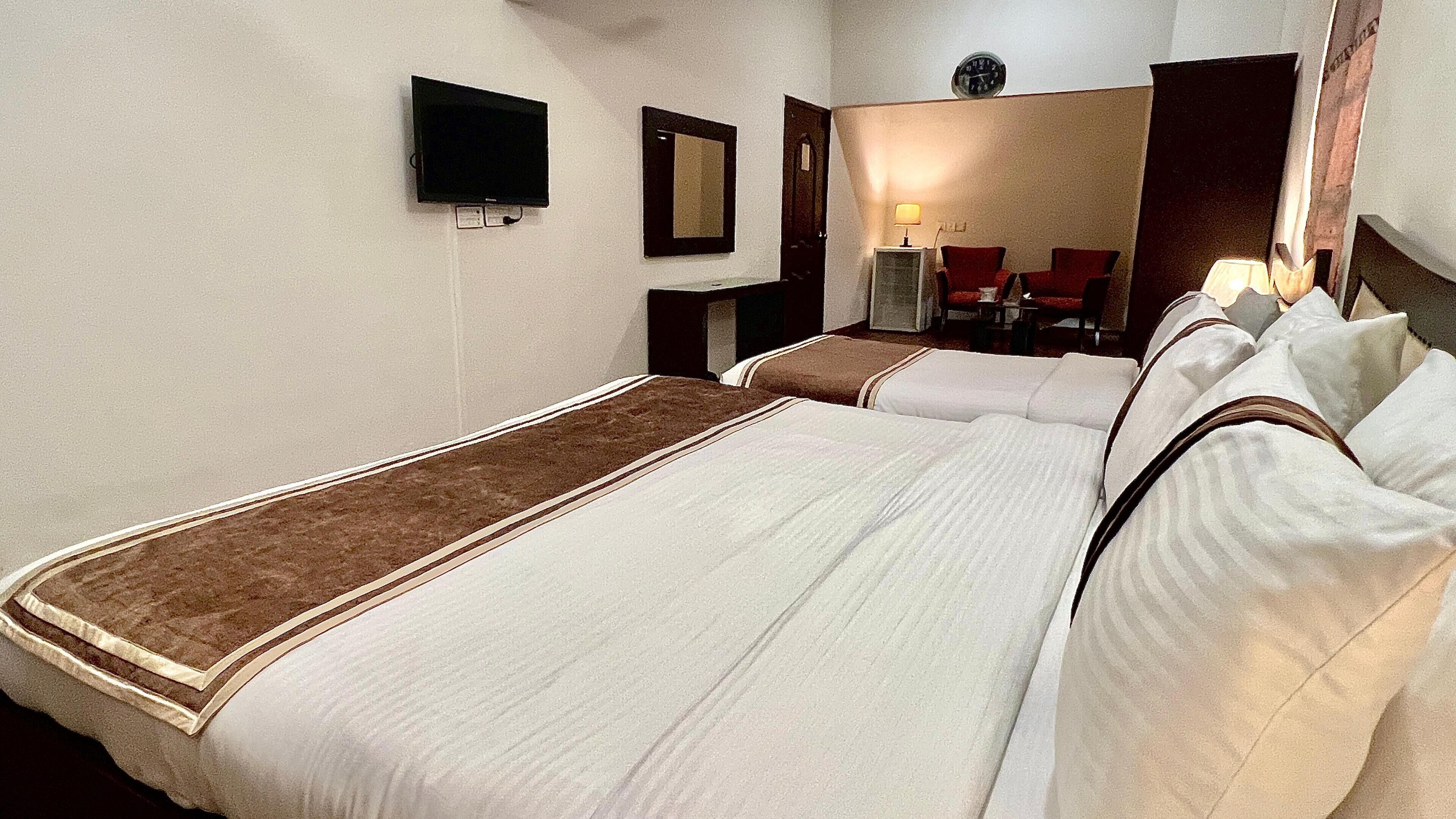 Habitación de hotel con una cama grande, un televisor de pantalla plana montado en la pared, un escritorio con una silla y un reloj en la pared.