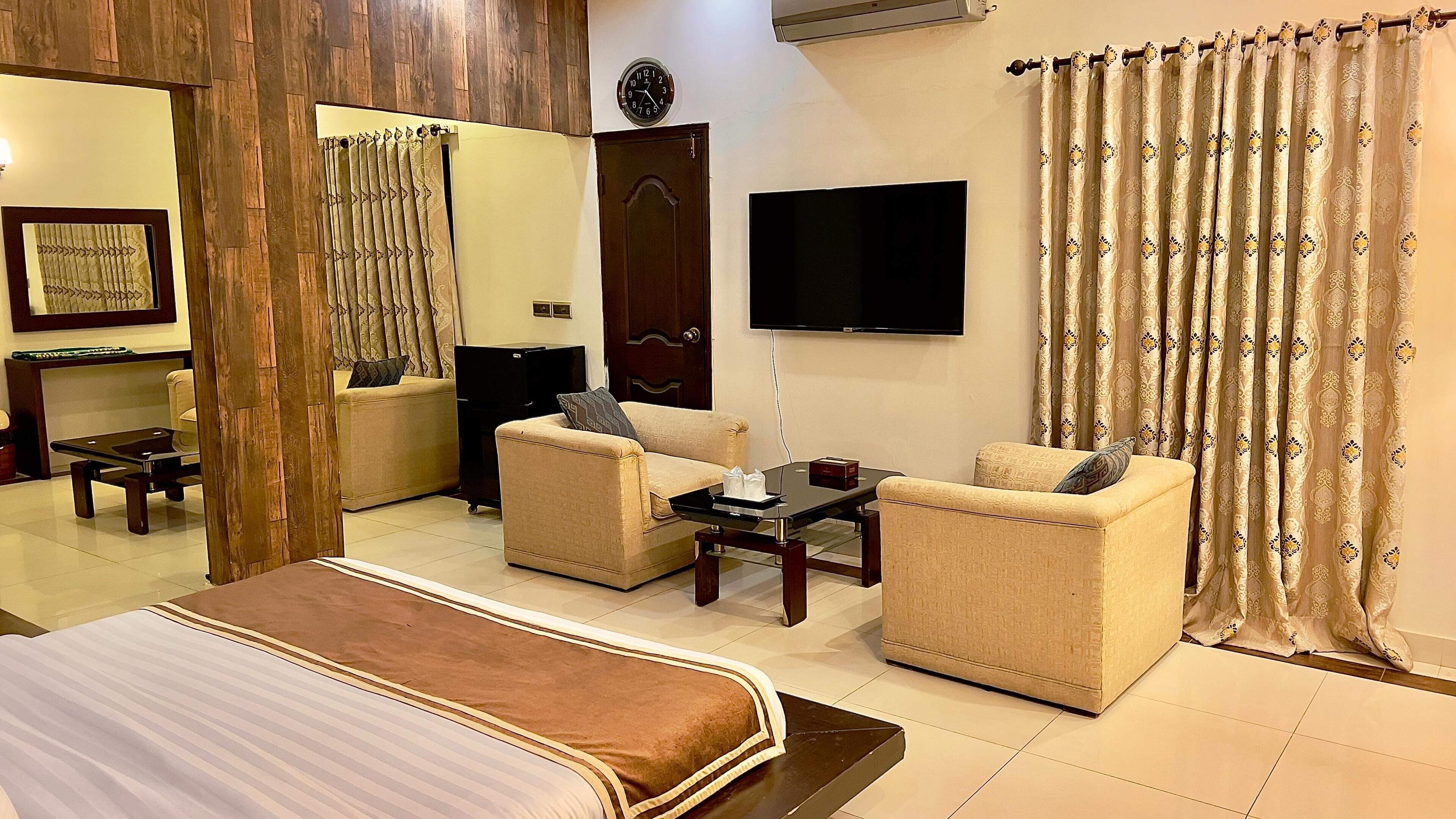 A hotel room with a bed, two armchairs, a coffee table, a TV, and a large window with curtains.