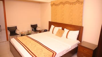 A neatly made bed with a patterned bedspread, a bedside table with a lamp, and a chair.