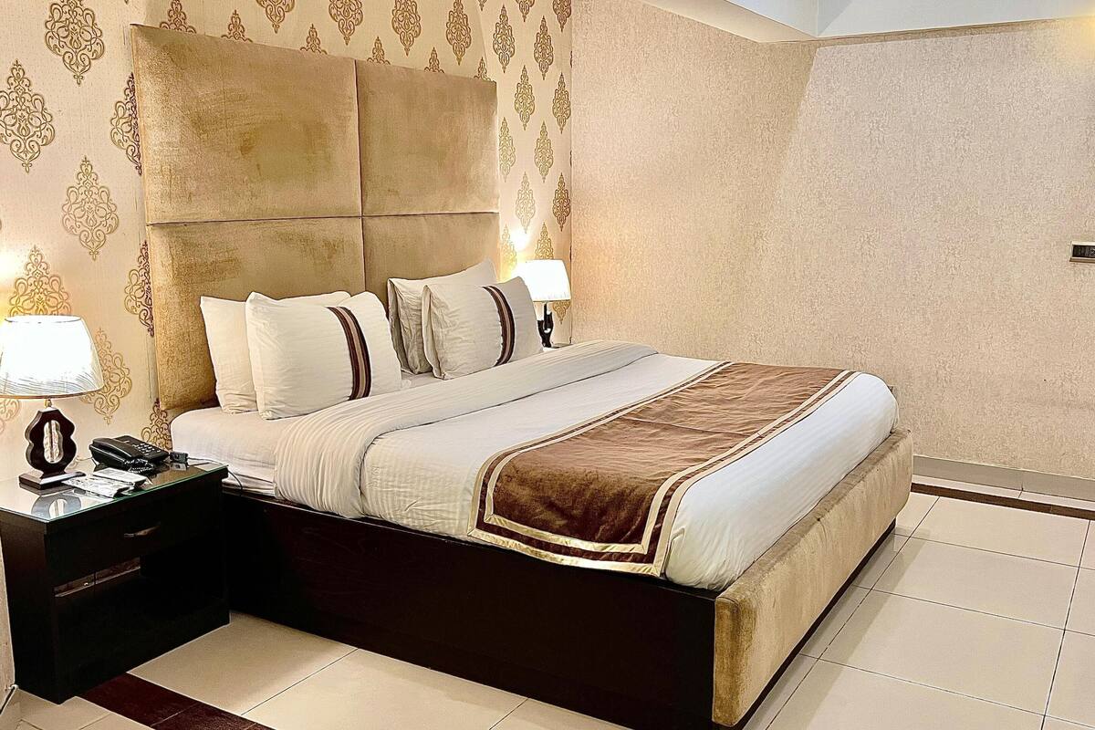 A hotel room with a large bed, two bedside lamps, a nightstand, and a door with a lock.