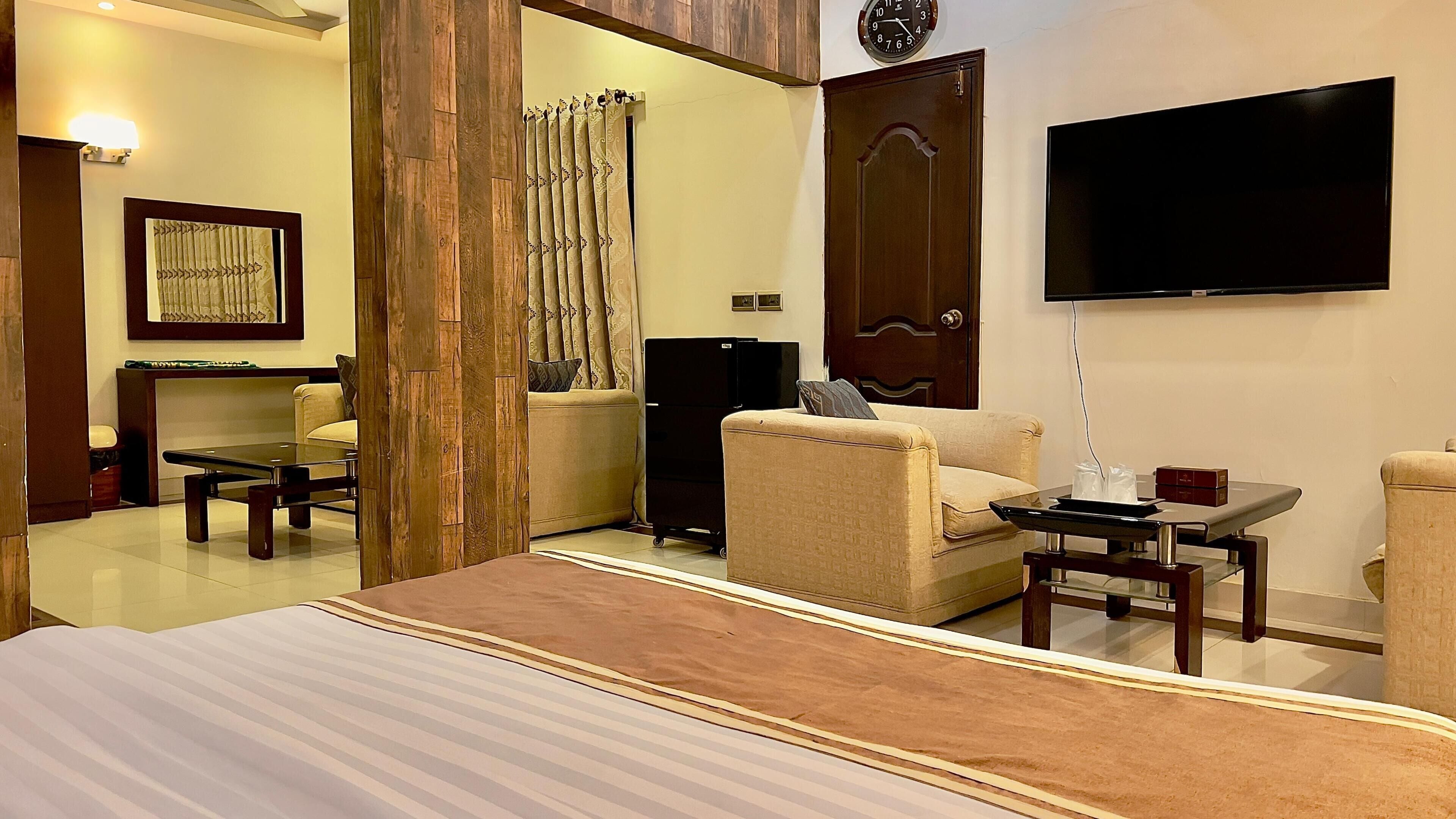 A hotel room with a bed, two sofas, a TV, a small table, and a refrigerator.