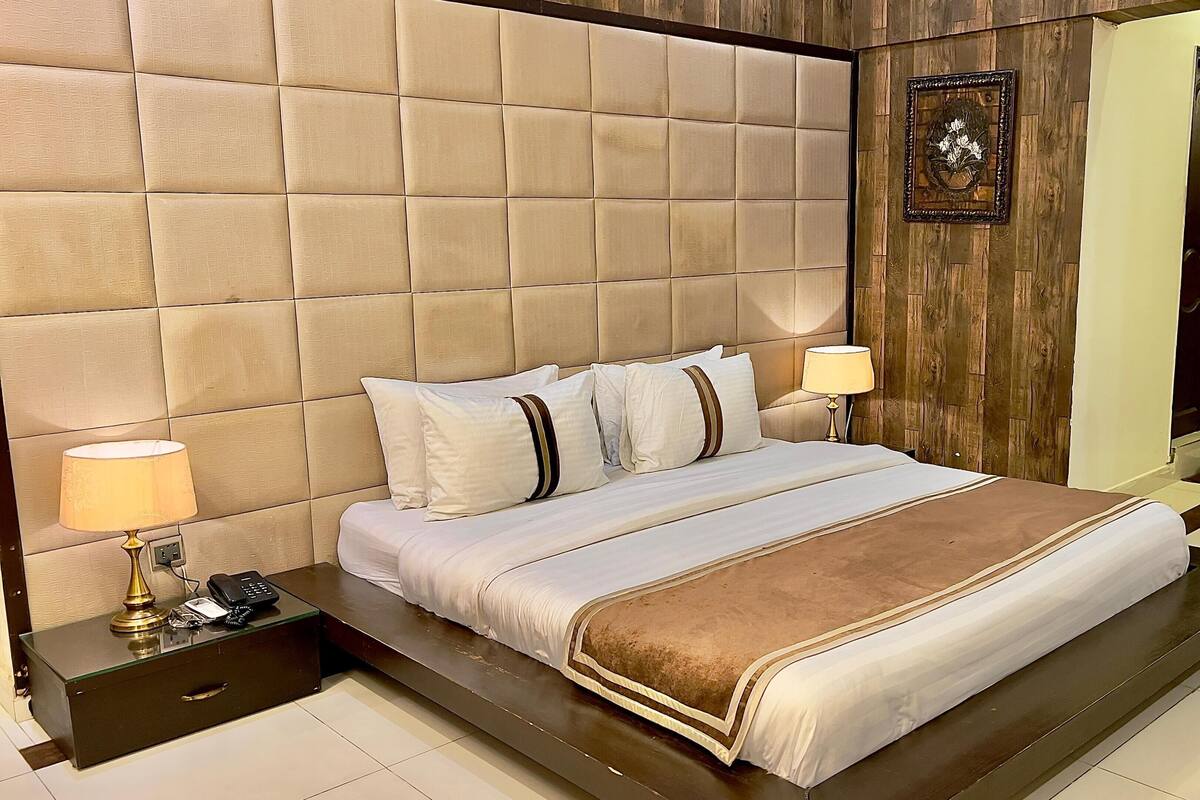 A bedroom with a tufted headboard, a bed with white and brown bedding, two bedside lamps, a bedside phone, and a small bedside table.