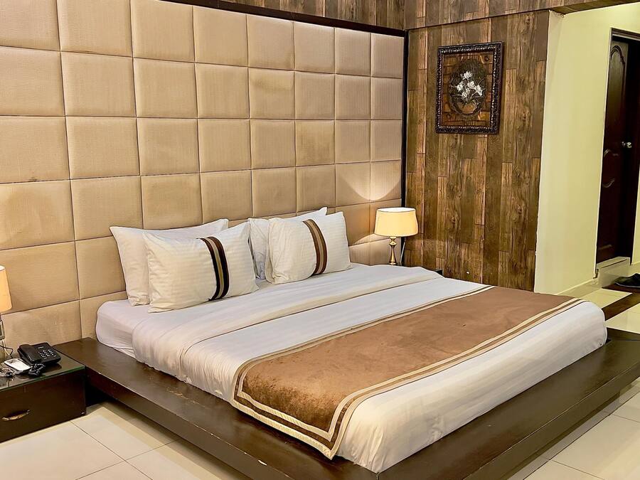 A bedroom with a tufted headboard, a bed with white and brown bedding, two bedside lamps, a bedside phone, and a small bedside table.