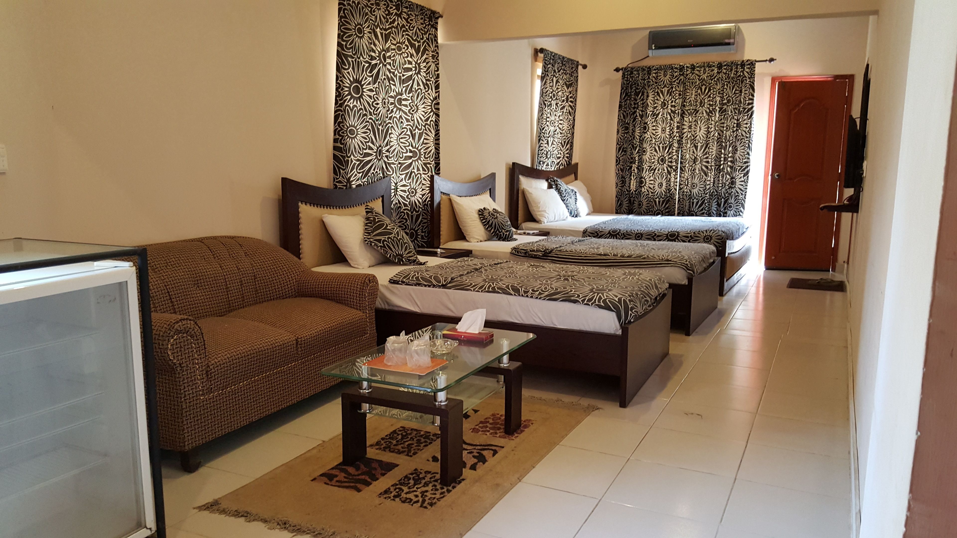 Habitación de hotel con sofá, dos camas, cortinas con estampado floral, una mesita de vidrio y un televisor.