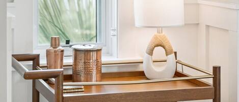 A wooden side table with a lamp and decorative items by a window.