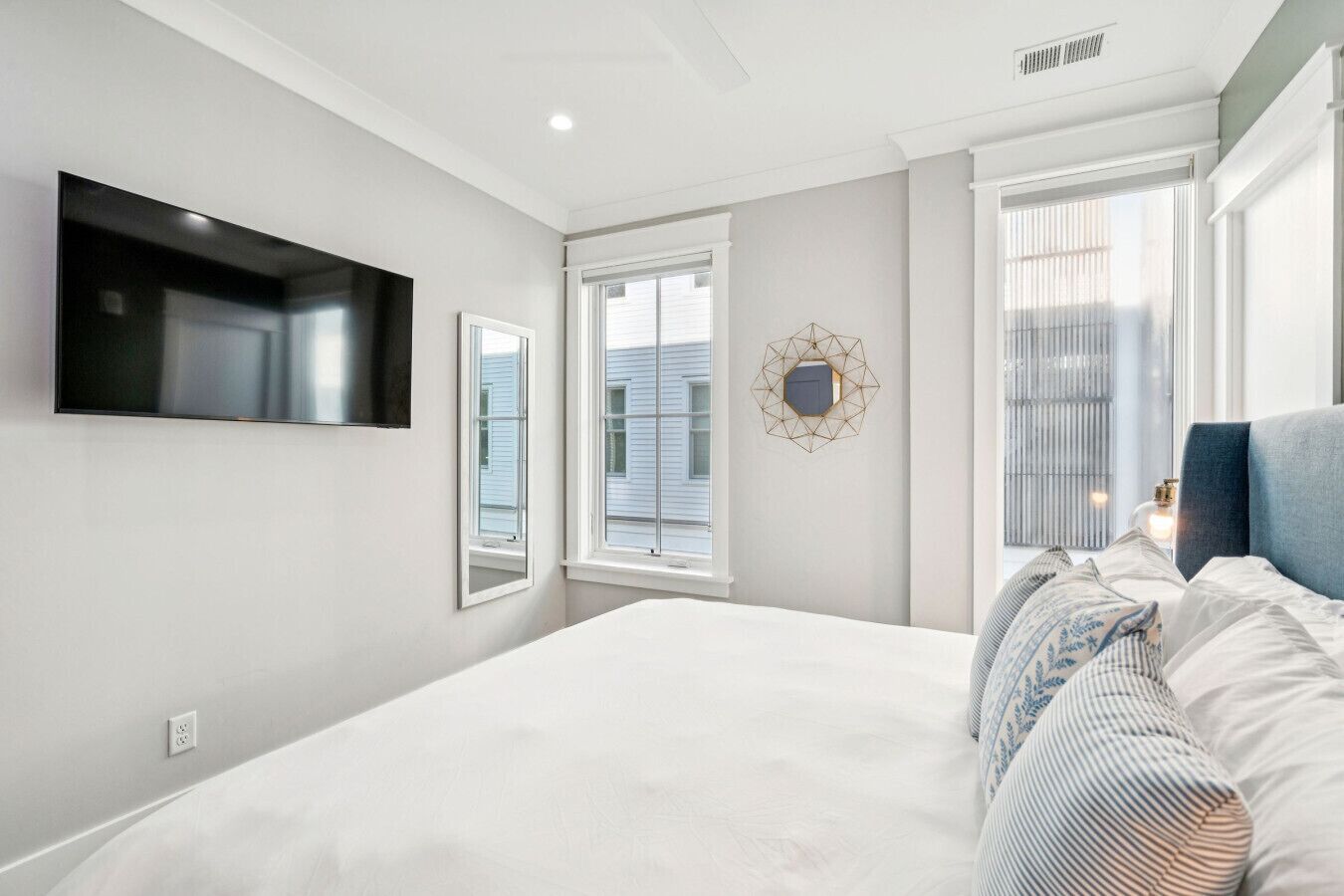A modern bedroom with a large bed, a flat-screen TV mounted on the wall, and a window with blinds.