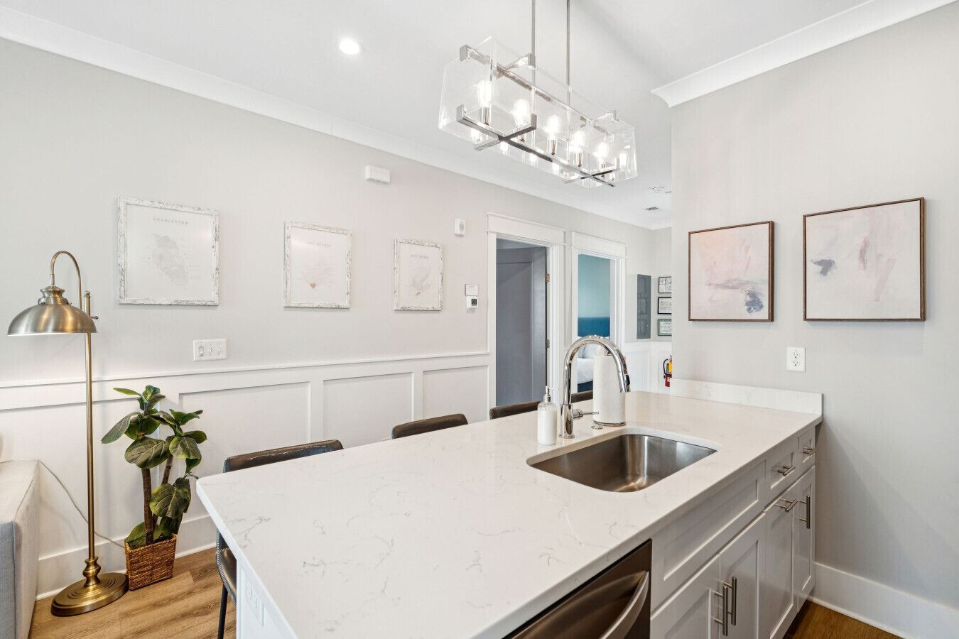 A modern kitchen with a large island, stainless steel sink, and pendant lighting.