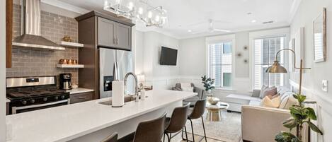 A modern kitchen with a central island, bar stools, a built-in oven, and a stainless steel range hood.