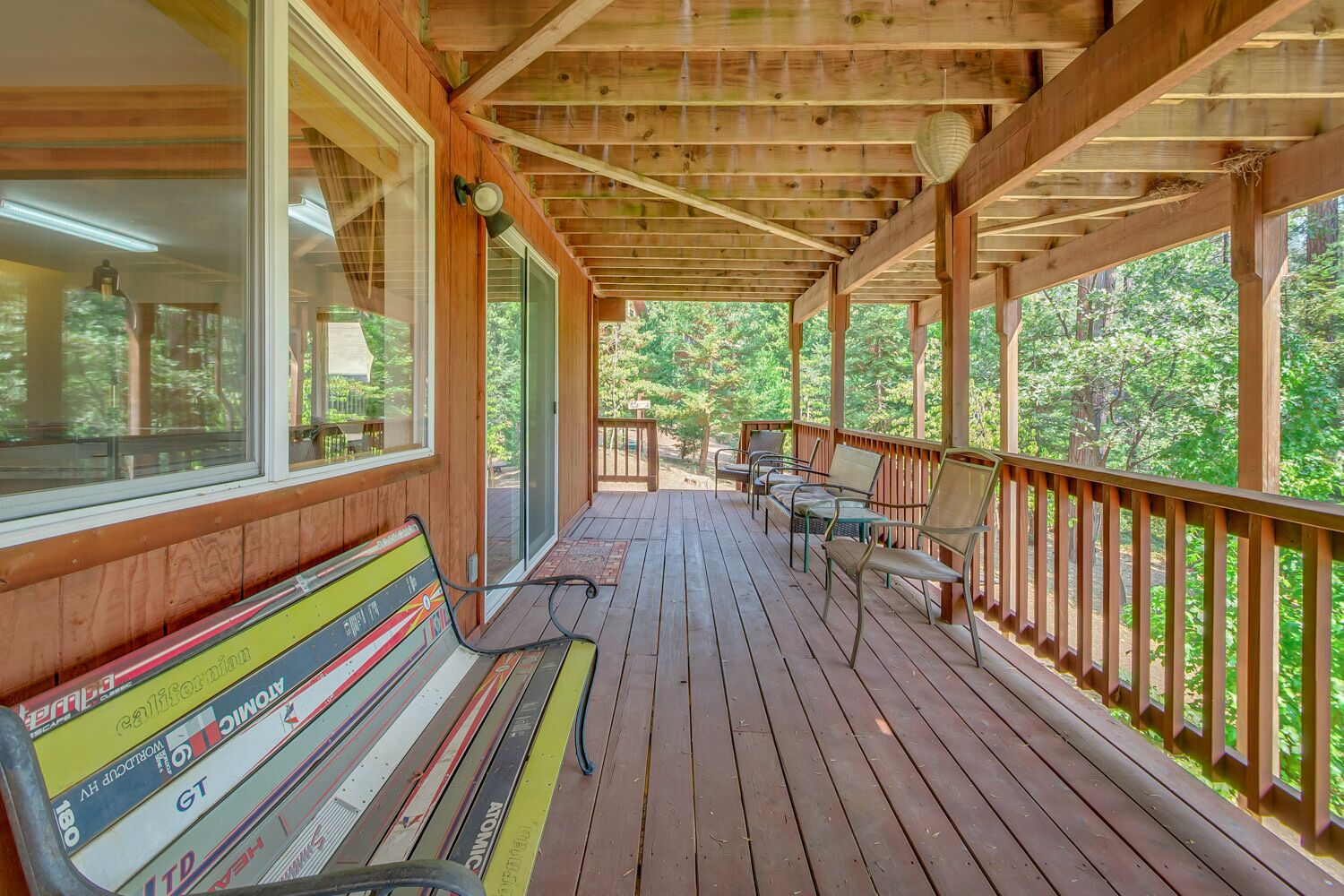 A wooden deck with a bench and chairs, overlooking a forested area.