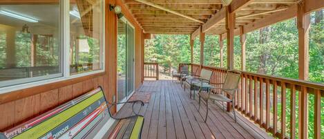 A wooden deck with a bench and chairs, overlooking a forested area.