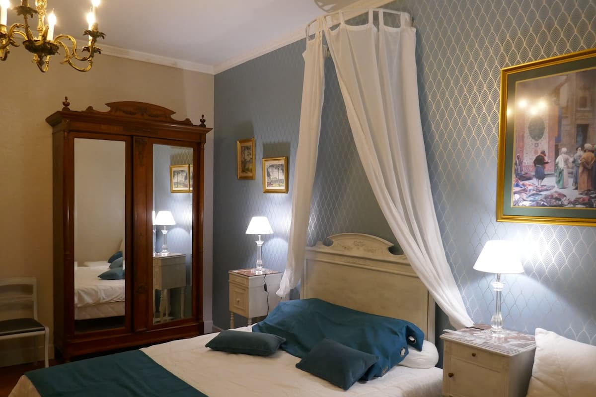 Quarto com cama, mesas de cabeceira, espelho, lustre e um quadro na parede.