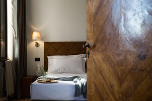 Una camera d'albergo con un letto, una lampada da comodino, una porta in legno e una finestra con tende.
