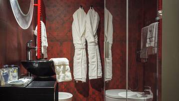 A bathroom with a black sink, a round mirror, a glass-enclosed shower, and two white towels hanging on the wall.