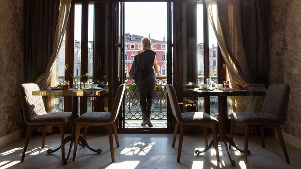 A room with a large window, a balcony, and a table with chairs.