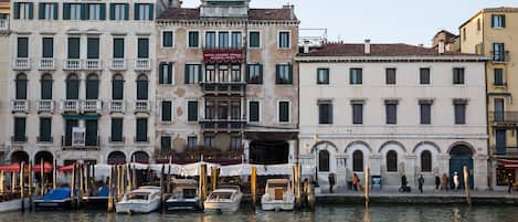 A canal with boats docked, historic buildings with balconies, and a clear sky.