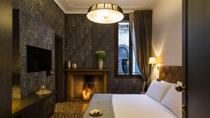 A hotel room with a bed, a fireplace, a television on the wall, and a window with curtains.