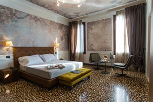 A hotel room with a large bed, a small sofa, a desk with a chair, and a patterned floor.