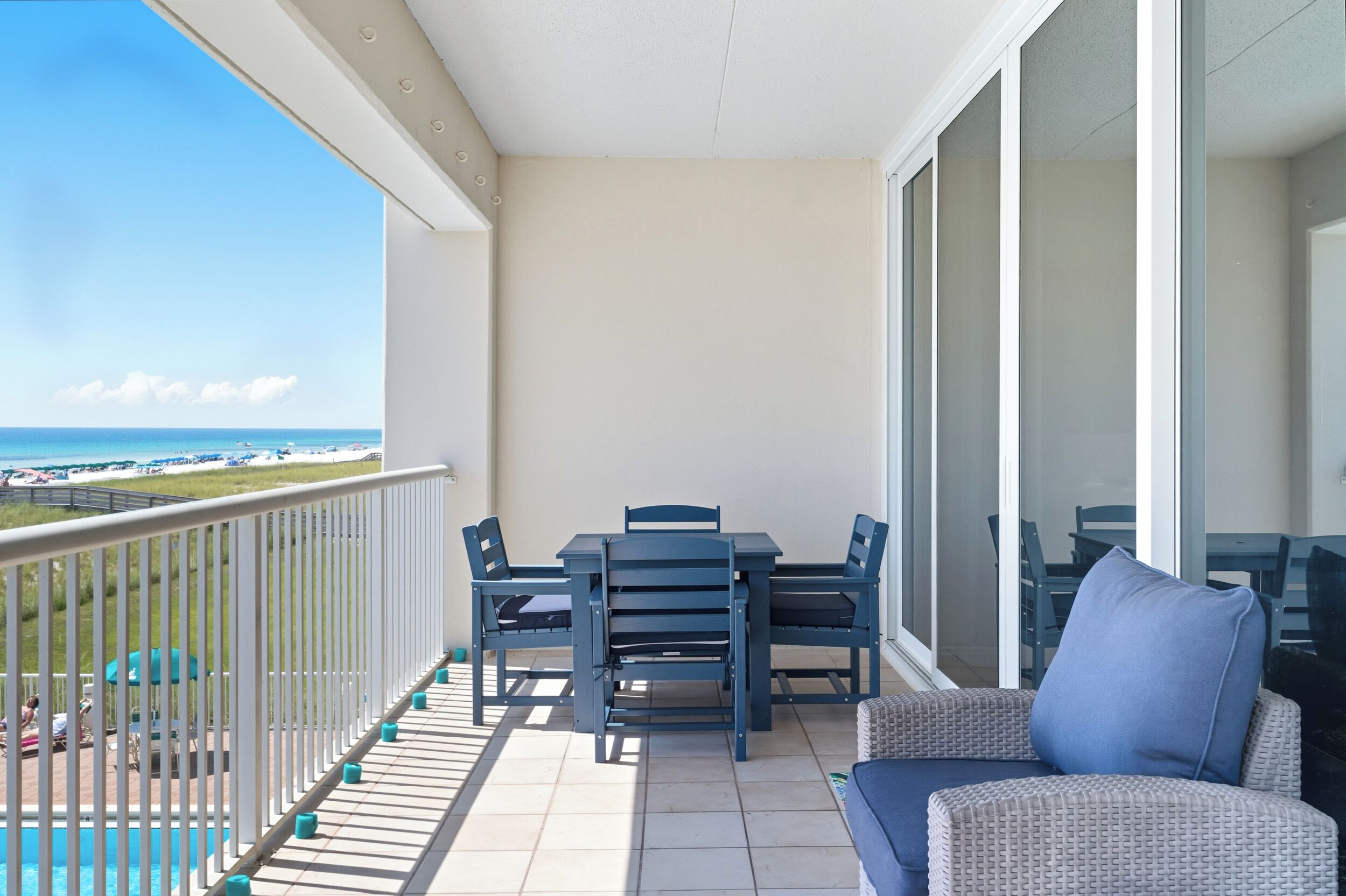 A balcony with a table and chairs, a sofa, and a view of the beach and ocean.