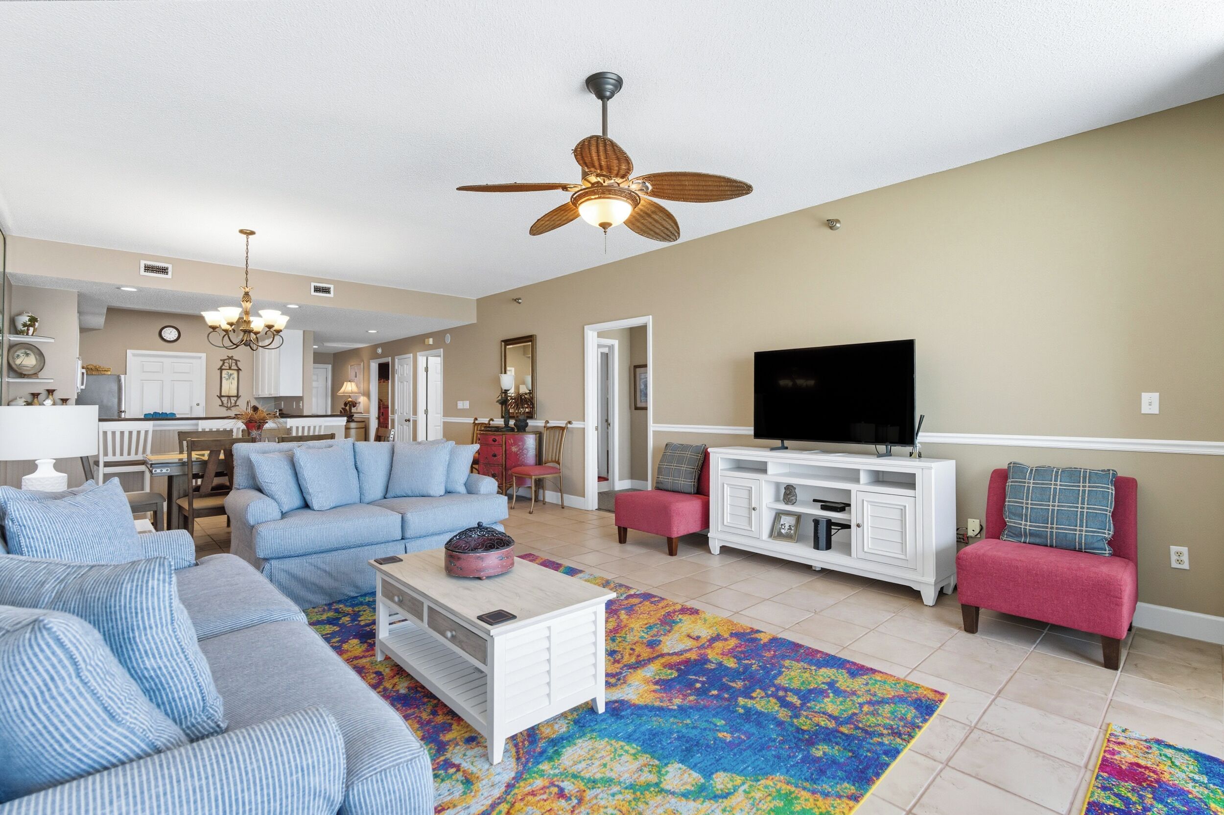 A spacious living room with a ceiling fan, a television, and a kitchen in the background.