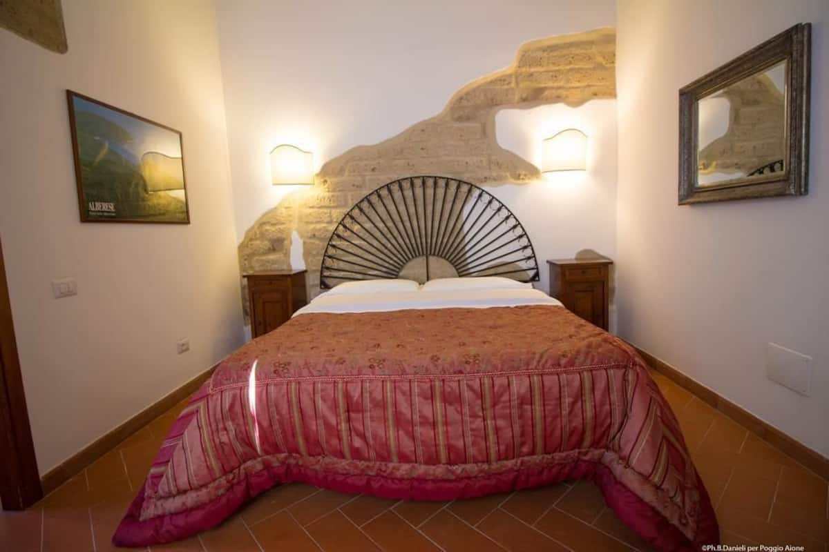 Une chambre à coucher avec un lit, un mur en pierre et deux lampes fixées au mur.