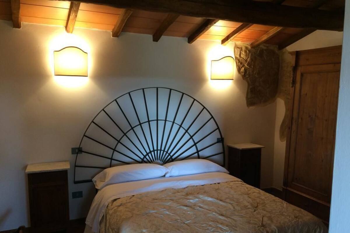 Une chambre à coucher avec une tête de lit incurvée, deux tables de chevet et une armoire en bois.
