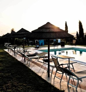 A poolside area with lounge chairs and umbrellas, a clear sky, and a calm pool.
