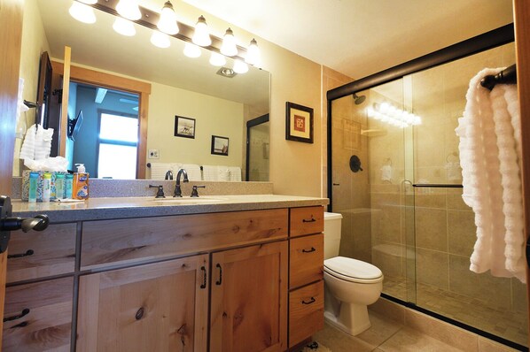 A bathroom with a wooden vanity, a large mirror, a toilet, and a glass-enclosed shower. - Top-Floor Alpine Getaway Ski-In/Out w/ Pool, Spa & Gym 1007 (Steamboat Springs)