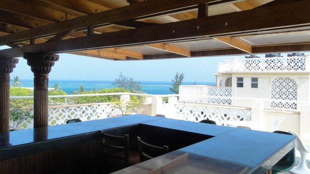 Un espacio al aire libre techado con bar y asientos, con vista al mar.