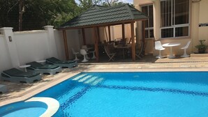 Piscina con sillas de descanso y un área de estar cubierta.