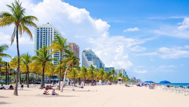 Ein Strand mit Palmen, einem Hotel und blauem Himmel.