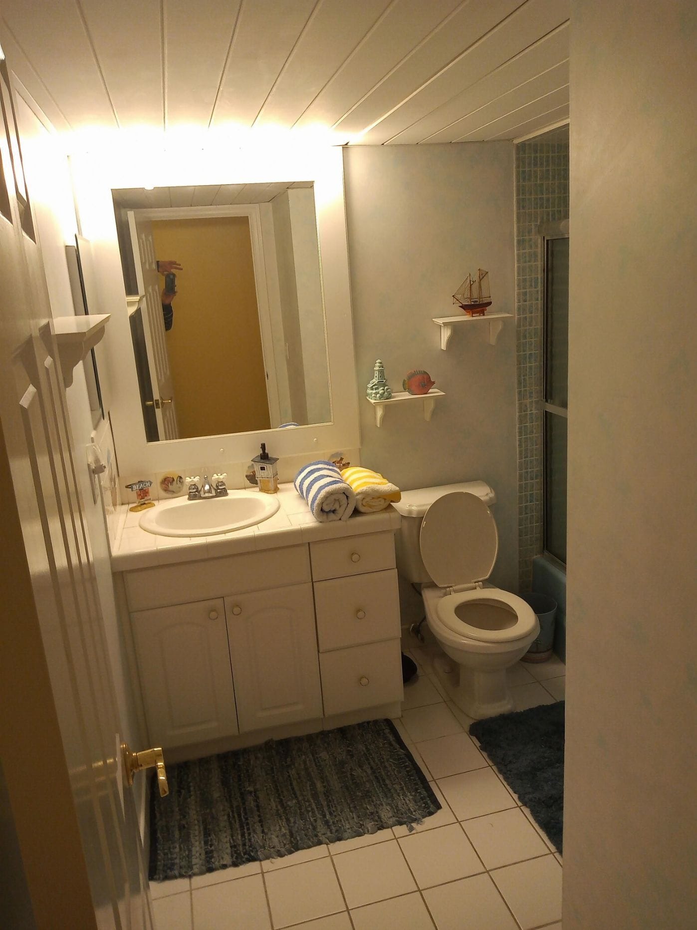 A bathroom with a white sink, mirror, and toilet. There are decorative items on the wall and a rug on the floor.