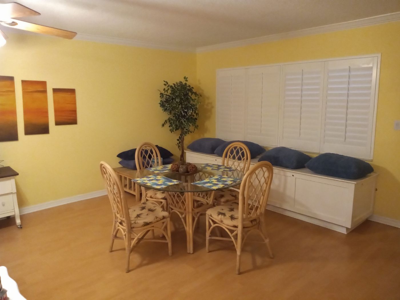 A dining area with a round table, four chairs, a potted plant, and a white cabinet with blue cushions.
