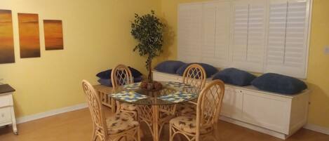 A dining area with a round table, four chairs, a potted plant, and a white cabinet with blue cushions.