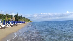 A beach with rows of blue umbrellas and lounge chairs along the shoreline. - Βίλα Μιχάλης  πανόραμα (Kombi)
